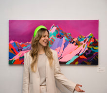 Load image into Gallery viewer, Artist Laura Jane Klassen wearing bright headband standing in the foreground of her Kiss and Freedom original mountain painting of the Tantalus Range by Whistler, BC. 
